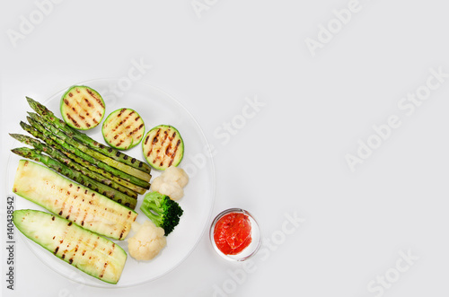 Grilled zucchini and asparagus, broccoli and cauliflower on a glass plate with red sauce