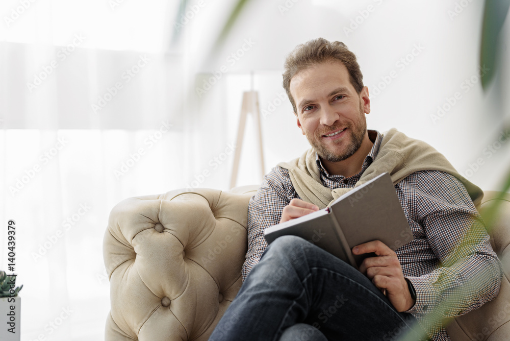 Cheerful man making notes into notebook
