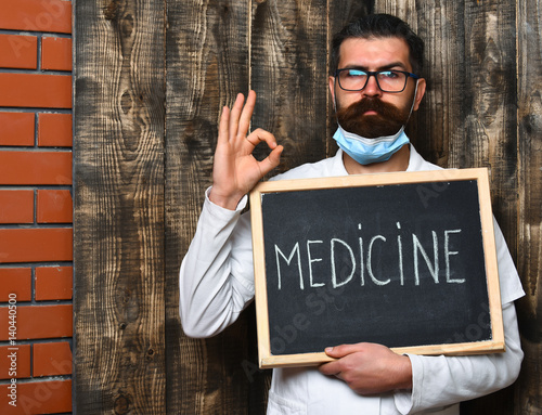 Bearded brutal caucasian doctor holding board with "Medicine" inscription
