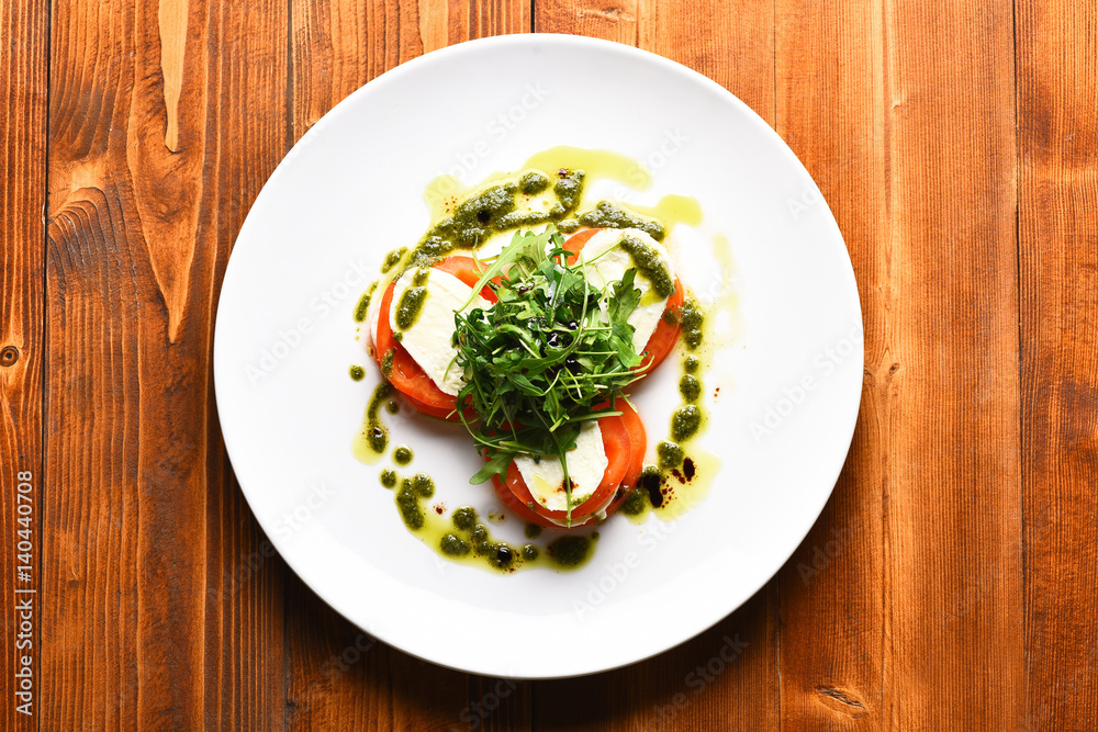 Tasty tomatoes sliced with mozarella cheese and green arugula salad Tasty tomatoes sliced with mozarella cheese and green arugula salad