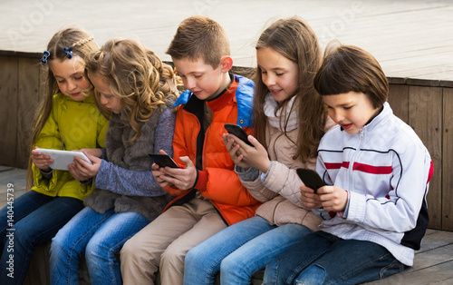 Laughing kids sitting with mobile devices
