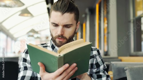 Handsome man in checked shirt reading interesting book in the cafe
 photo