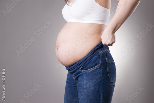 Pregnant woman in blue jeans for pregnant women on gray background
