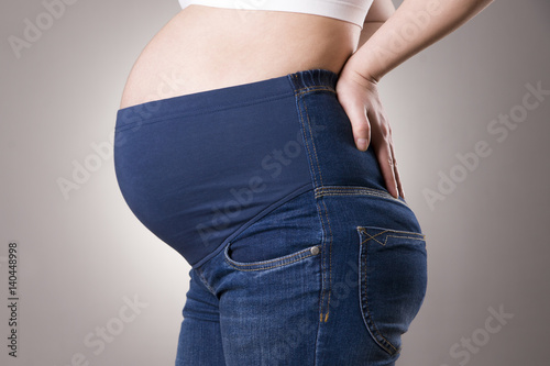 Pregnant woman in blue jeans for pregnant women on gray background © staras