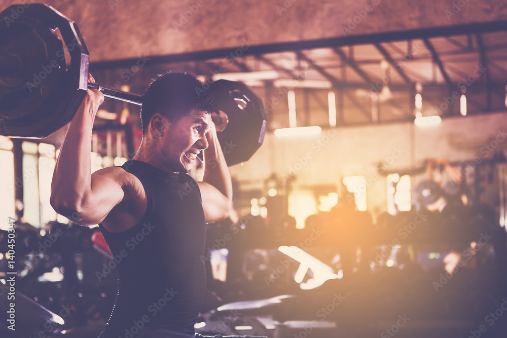 Fototapeta premium handsome young muscular sports man lifting weights at the gym looking serious