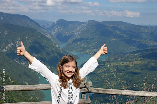 happy little girl with thumbs up on mountain top