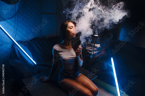 Closeup Young, beautiful girl smoke a hookah at club. Sexy woman smoking. Fashion