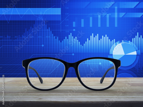 Black eye glasses on wooden table over financial graph and chart, Business vision concept