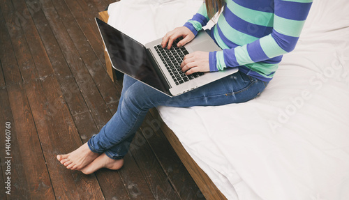 The young woman is sitting on the bed with a laptop