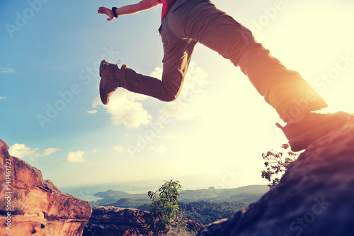 jumping over precipice between two rocky mountains at sunset. freedom, risk, challenge, success concept