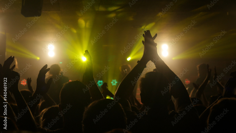 Fans waving their hands at rock concert in night club on beautiful golden lights