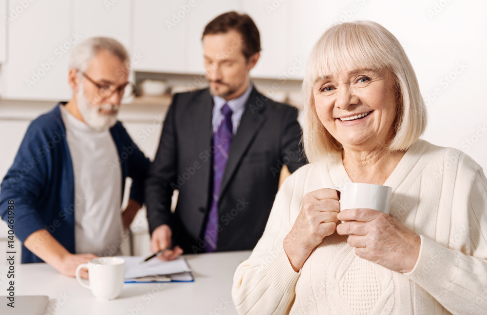 Glad elderly woman relaxing while her husband meeting with lawyer Glad elderly woman relaxing while her husband meeting with lawyer