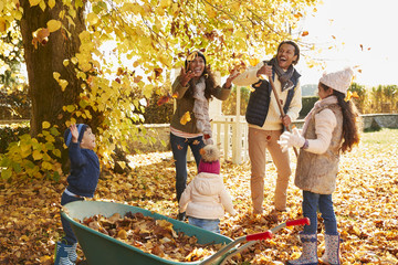 Children Helping Parents To Collect Autumn Leaves In Garden