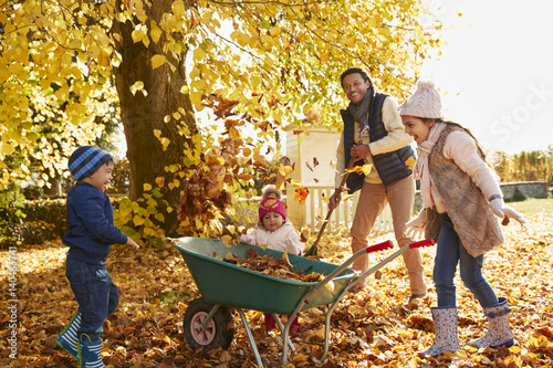 Children Helping Father To Collect Autumn Leaves In Garden