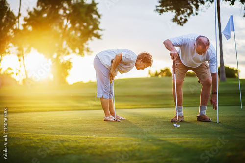 active senior lifestyle, elderly couple playing golf together at sunset