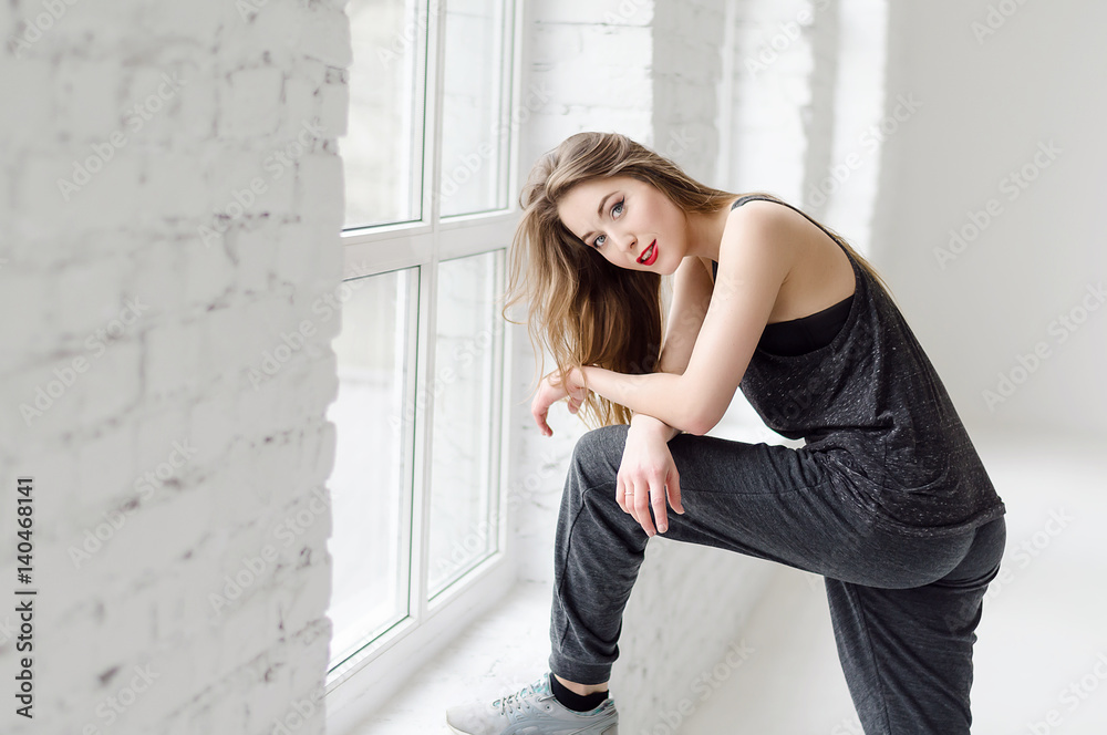 Photo of young attractive model woman in studio with big windows. Model wearing sporty clothes, fashion concept