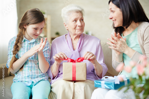 Senior woman with packed gift looking at her daughter clapping hands