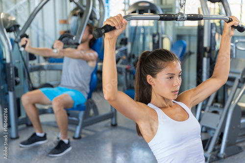 Shoulder pull down machine. Fitness girl training chest muscles at gym.