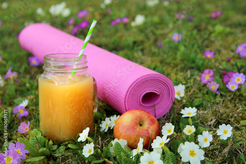 Yoga mat on green grass with flowers. Jar with juice. Spring. Apple. Concept of sports. selective focus.