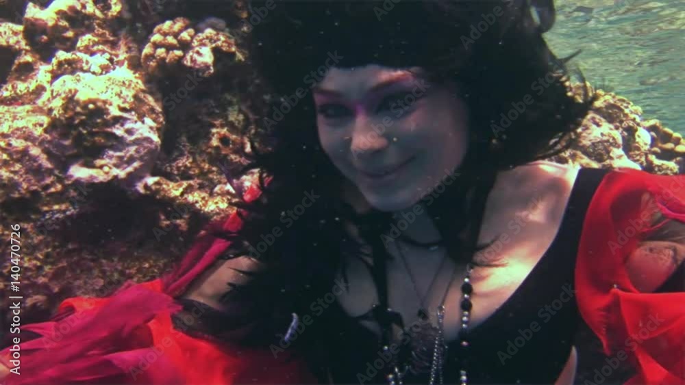 Young girl model free diver underwater in red costume of pirate in Red Sea. Filming a movie. Actress smiling at camera. Extreme sport in marine landscape, coral reefs, ocean inhabitants. Young girl model free diver underwater in red costume of pirate in Red Sea. Filming a movie. Actress smiling at camera. Extreme sport in marine landscape, coral reefs, ocean inhabitants.