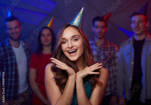 Cheerful girl in birthday cap on background of her friends