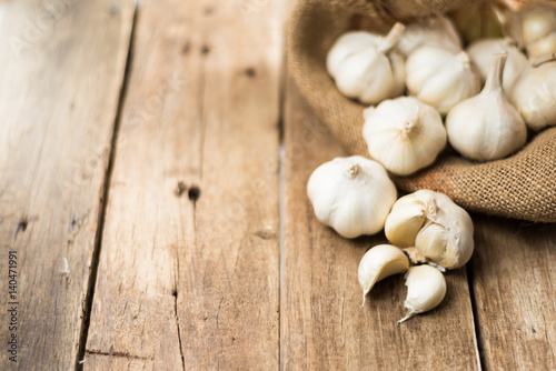 peeled white garlic in gunny sack cloth on brown wooden table with copy space, selective focus