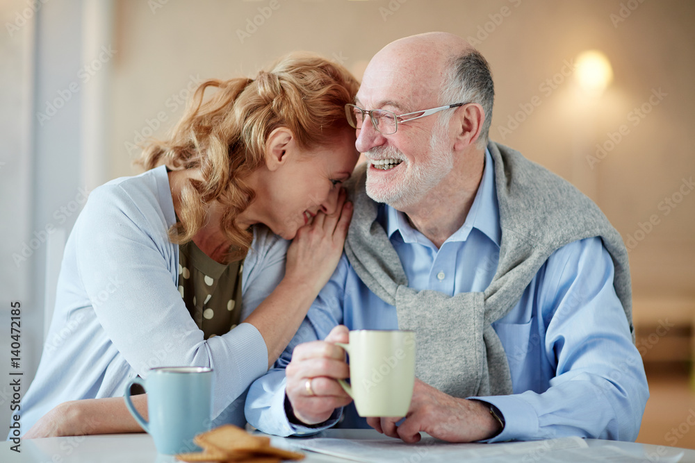 Portrait of smiling senior couple sitting close together cuddling caringly and laughing
at kitchen table with tea cups and homemade cookies Portrait of smiling senior couple sitting close together cuddling caringly and laughing
at kitchen table with tea cups and homemade cookies