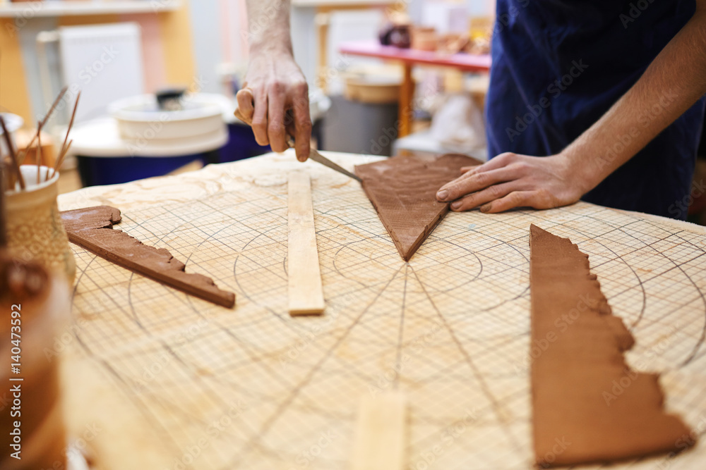 Professional potter using paper diagram while cutting clay workpiece Professional potter using paper diagram while cutting clay workpiece