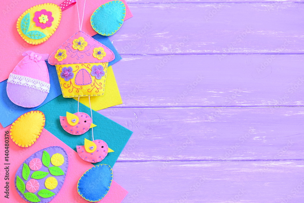 Children Easter background. Handmade vibrant felt Easter crafts on lilac wooden background with empty copy space for text. Felt house ornament, felt eggs ornaments set. Top view