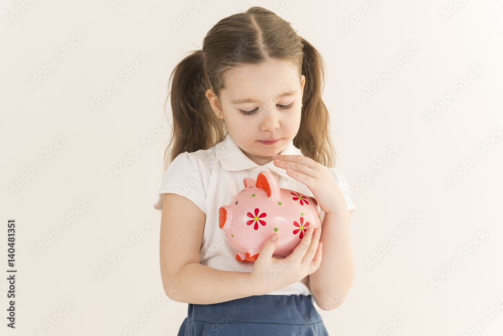 Close up portrait of happy young little girl snuggling pink piggy bank. Education, school and money saving concept. Junior Savings Account concept Close up portrait of happy young little girl snuggling pink piggy bank. Education, school and money saving concept. Junior Savings Account concept