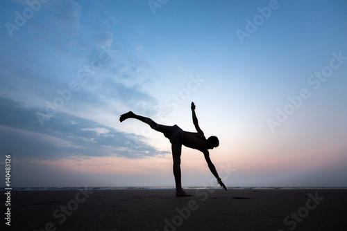 Young healthy man practicing yoga on the beach at sunset