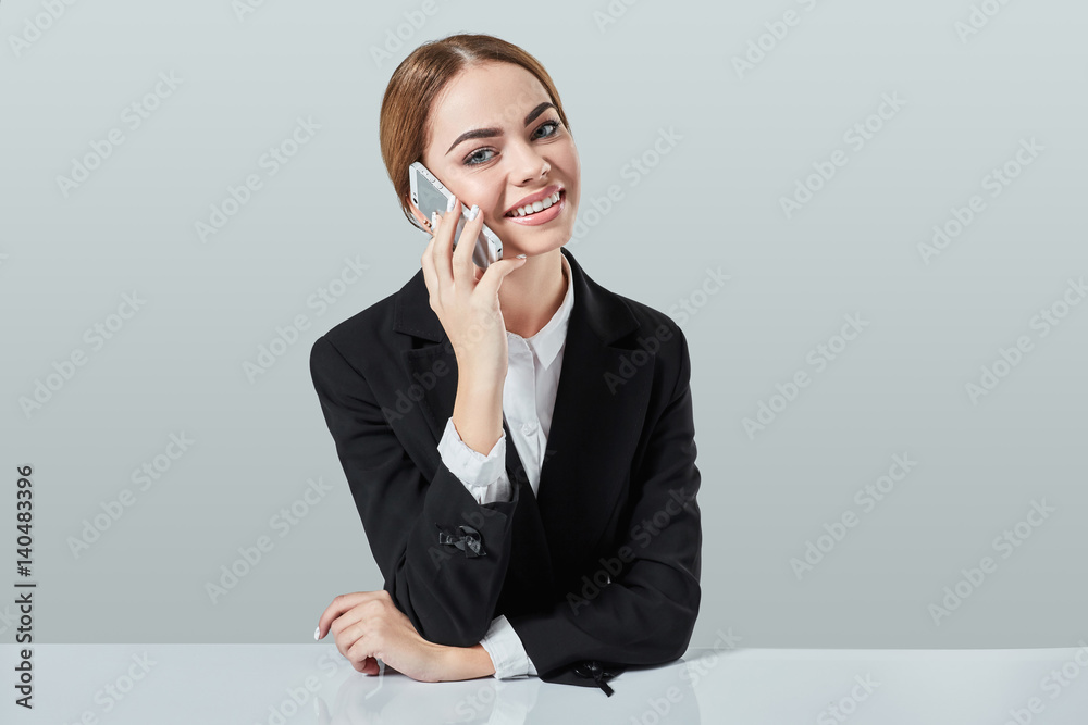 attractive dark-haired woman dressed in a black suit is sitting at table in an office. attractive dark-haired woman dressed in a black suit is sitting at table in an office.