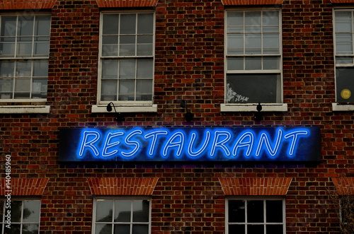 Glowing neon letter on brick wall saying restaurant. The text restaurant is written using image processing software. It consist 6 layers