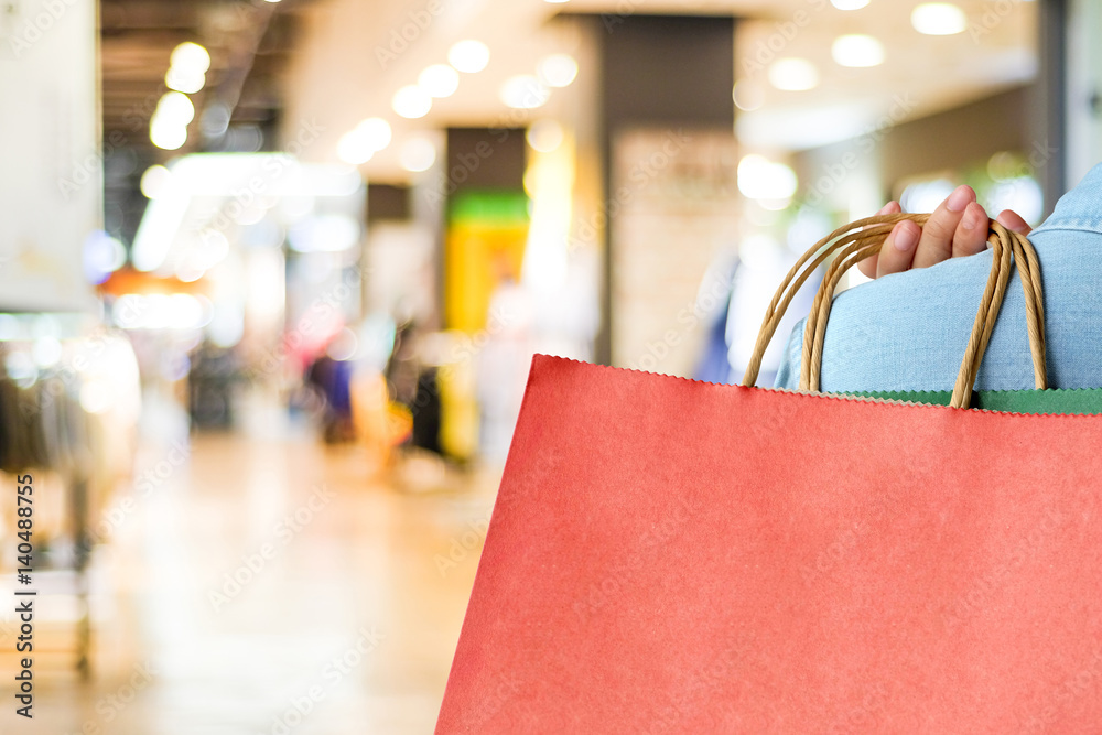 Naklejka premium Hand holding red shopping bag on blur store background with copy space for text, template, business concept