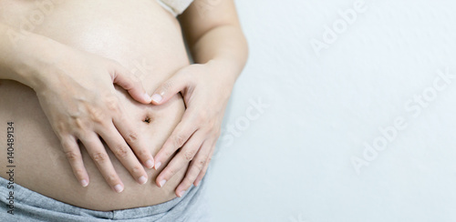 Closeup of Belly of a pregnant woman,pregnant woman holding her hands on her swollen belly shaping a heart, toned retro or vintage effect.selective focus