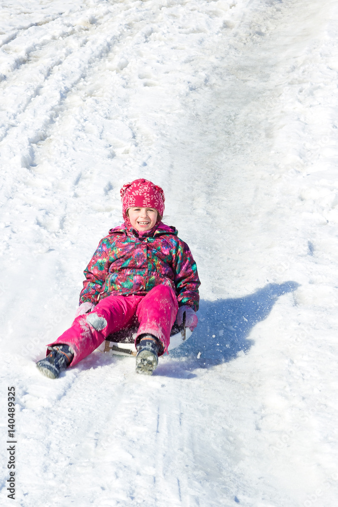 Happy child sliding from a snowy hill. Active winter leisure outdoors