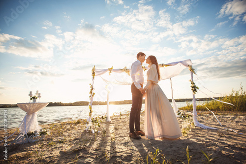 Couple in love holding hands near decorations and arch for wedding ceremony on beach. Honeymoon at sea side of ocean