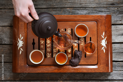 Tea in cups, glass jug and human hand pouring tea