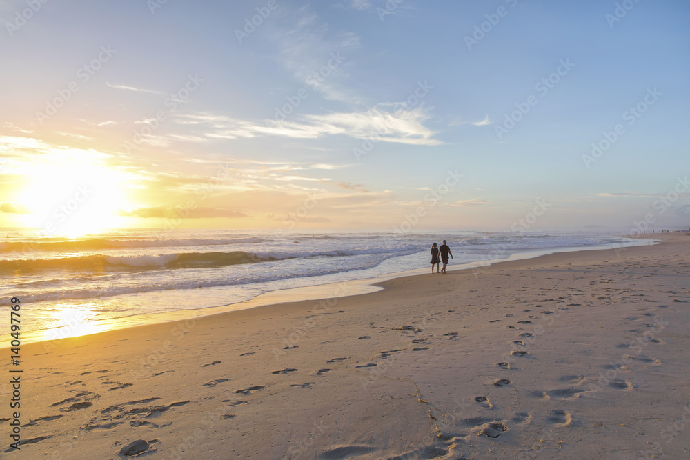 Naklejka premium People walking on a beach into the distance, as the sunrises over the ocean