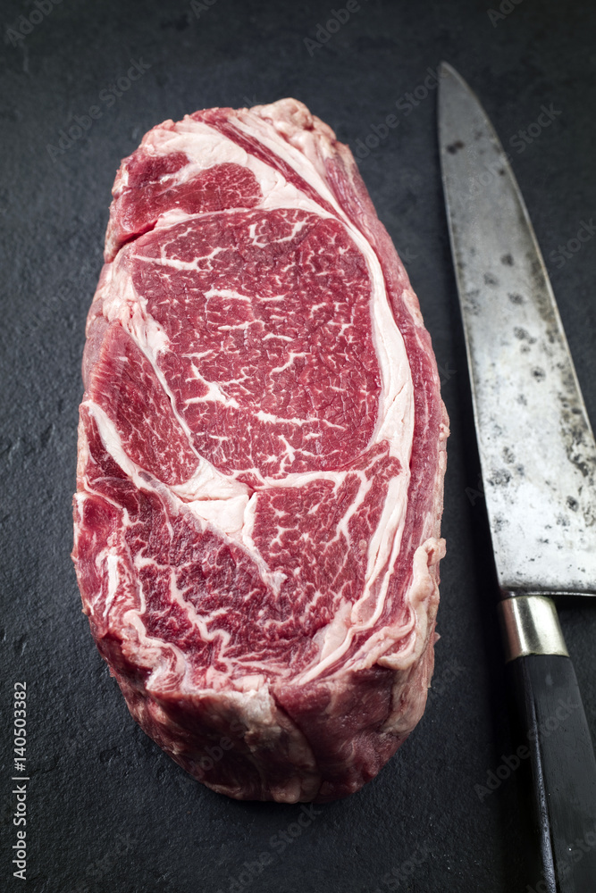 Raw dry aged Wagyu Rib Eye Steak with Knife on a slate