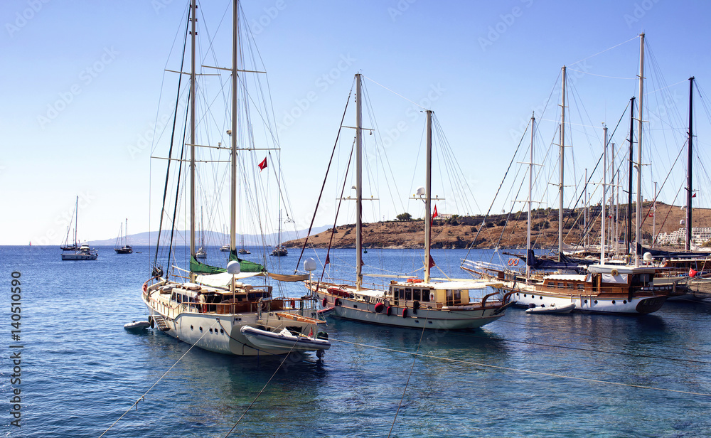 Luxury yachts (sailing boats) parked on turquoise water in front of Bodrum castle. The image shows Aegean and Mediterranean culture of coastal lifestyle.