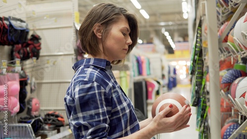 Young woman selecting sport equipment in supermarket. Choosing ball for soccer or football