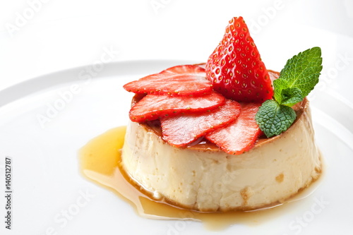  Milk pudding with caramel and strawberries on a white plate 