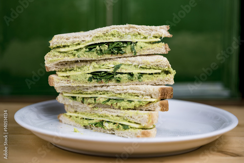 Quartered and stacked avocado and fresh lettuce sandwich on a white plate viewed from the side