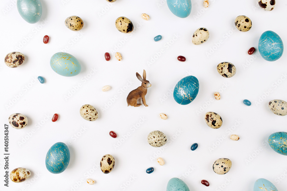 Easter holiday concept with  quail and blue Easter eggs,  bunny, and candies  on white background. Flat lay, top view. Easter concept.