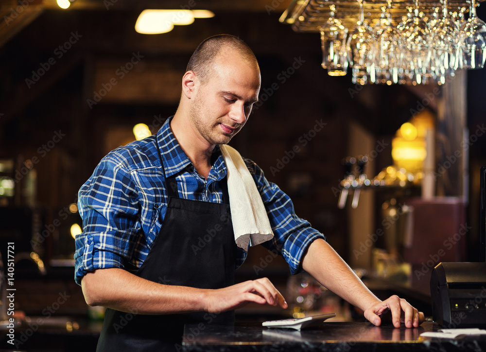 Barman at work in pub,Portrait of cheerful barman worker standing,Waiter giving menus,A pub.Bar.Restaurant.Classic.Evening.European restaurant.European bar.American restaurant.American bar. Barman at work in pub,Portrait of cheerful barman worker standing,Waiter giving menus,A pub.Bar.Restaurant.Classic.Evening.European restaurant.European bar.American restaurant.American bar.