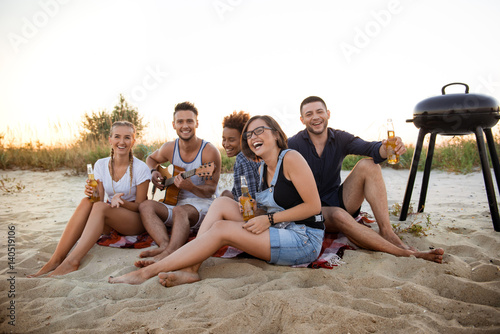 Young company of friends rejoicing, resting at beach during sunrise.