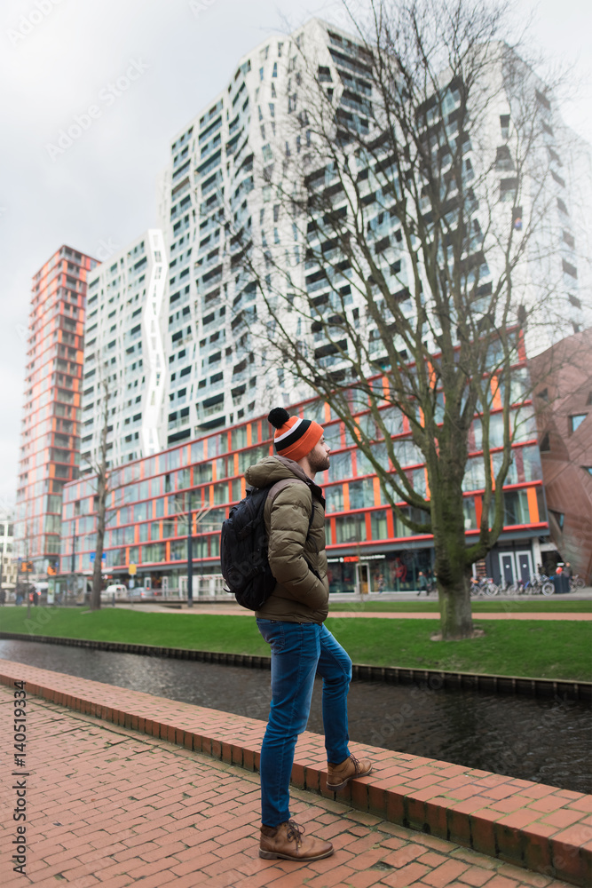 A young guy dressed warmly examines the city in the morning in rainy weather. Rotterdam, Netherlands.