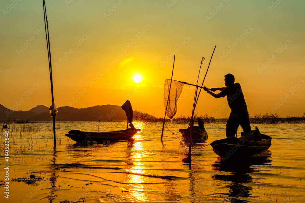 Silhouette of fishermen using nets to catch fish at the lake during sunset time