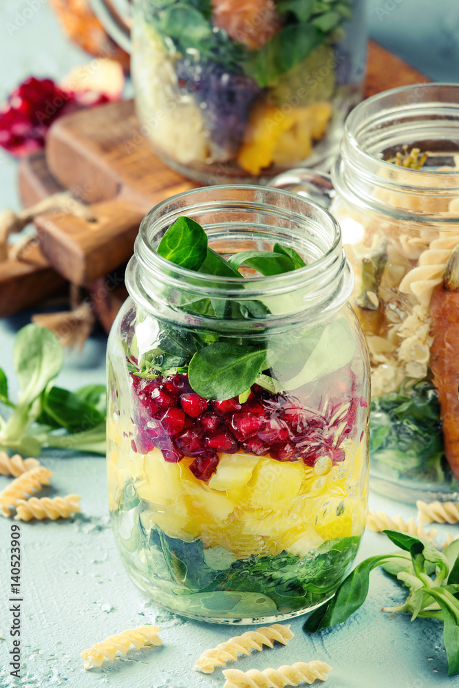 Variety of salads in mason jars. Fruit salad mango, pomegranate, greens, vegetables, wholegrain pasta, carrots and cauliflower, salmon. Standing over blue texture background. Food to go. Variety of salads in mason jars. Fruit salad mango, pomegranate, greens, vegetables, wholegrain pasta, carrots and cauliflower, salmon. Standing over blue texture background. Food to go.
